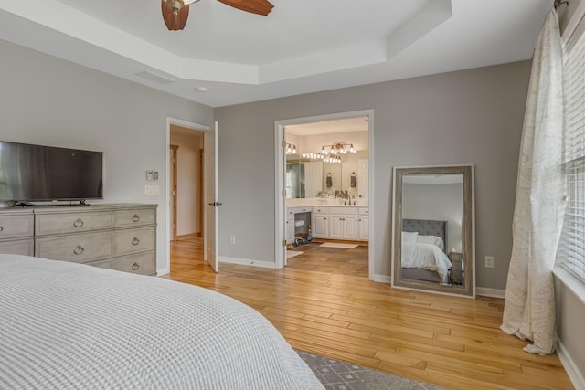 bedroom with ceiling fan, ensuite bathroom, a raised ceiling, sink, and light hardwood / wood-style flooring