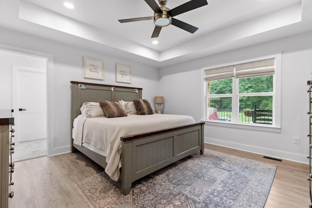 bedroom featuring visible vents, baseboards, a raised ceiling, and light wood finished floors