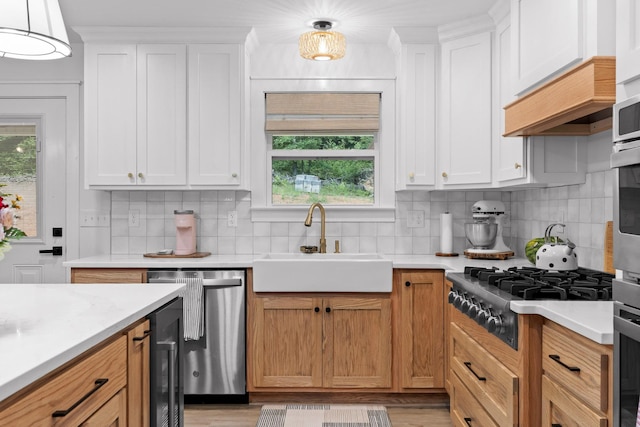 kitchen featuring a sink, backsplash, white cabinetry, stainless steel appliances, and light countertops