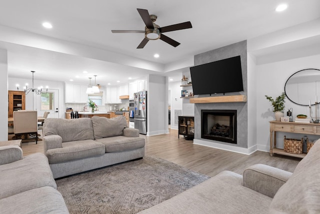 living room with baseboards, recessed lighting, light wood-style floors, ceiling fan with notable chandelier, and a large fireplace