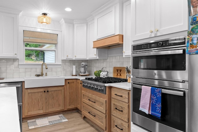 kitchen featuring stainless steel appliances, a sink, light countertops, white cabinetry, and tasteful backsplash