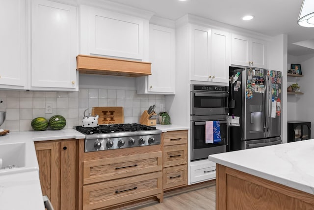 kitchen with decorative backsplash, light wood-style floors, appliances with stainless steel finishes, and white cabinets