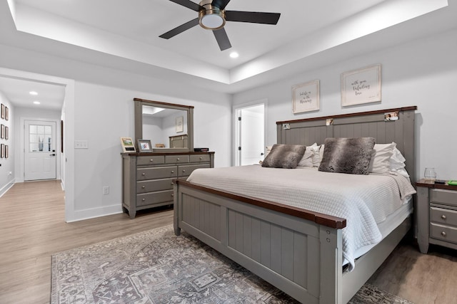 bedroom with a raised ceiling, wood finished floors, recessed lighting, baseboards, and ceiling fan