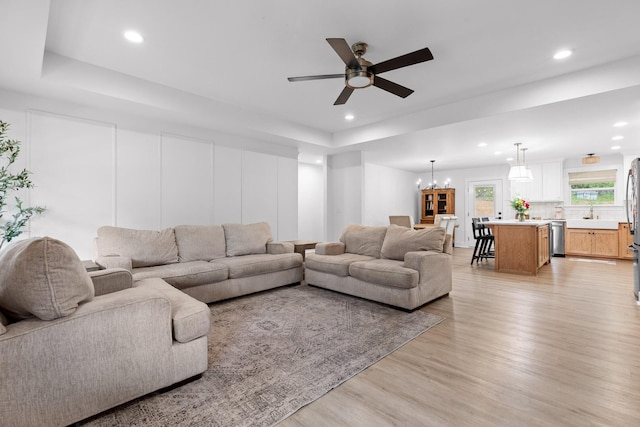 living area featuring recessed lighting, a tray ceiling, light wood finished floors, and ceiling fan with notable chandelier