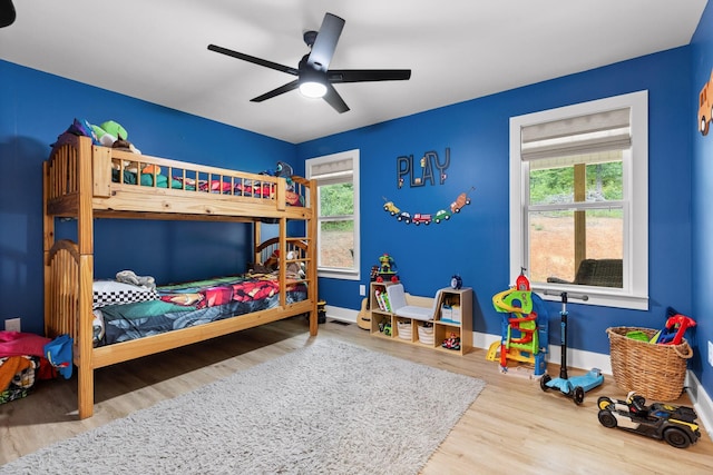 bedroom featuring ceiling fan, baseboards, multiple windows, and wood finished floors