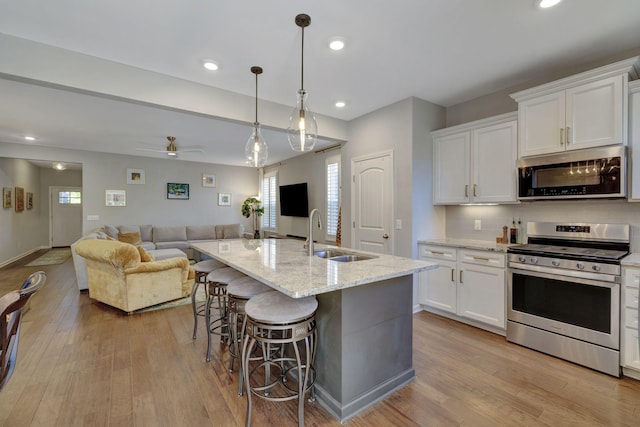 kitchen with stainless steel appliances, white cabinets, decorative light fixtures, and an island with sink