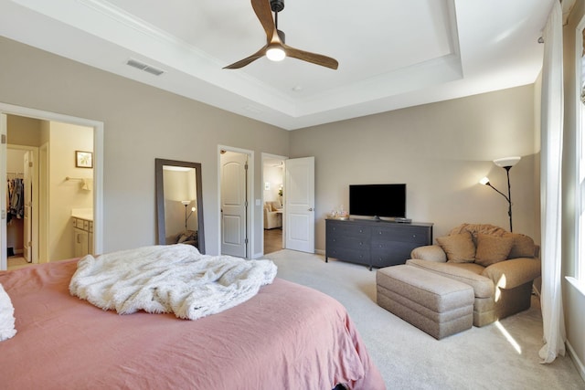 bedroom with ceiling fan, connected bathroom, a raised ceiling, light colored carpet, and a walk in closet