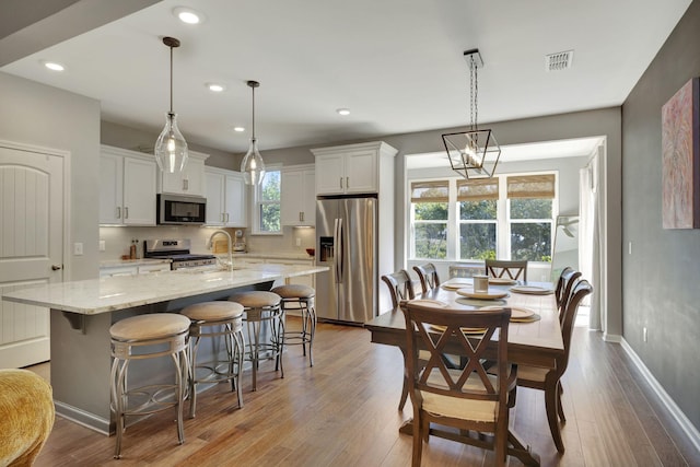 kitchen featuring pendant lighting, white cabinets, appliances with stainless steel finishes, a kitchen island with sink, and a breakfast bar area