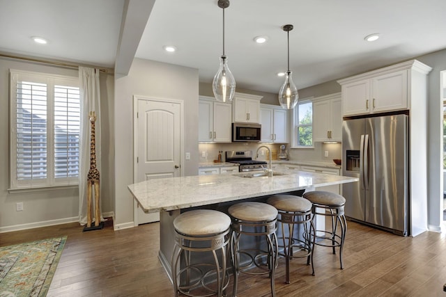 kitchen with decorative light fixtures, a center island with sink, light stone countertops, appliances with stainless steel finishes, and white cabinets