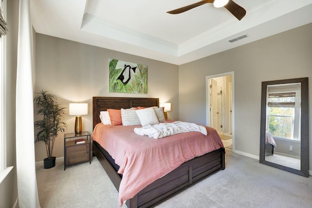 bedroom with light carpet, ceiling fan, a raised ceiling, and ensuite bath