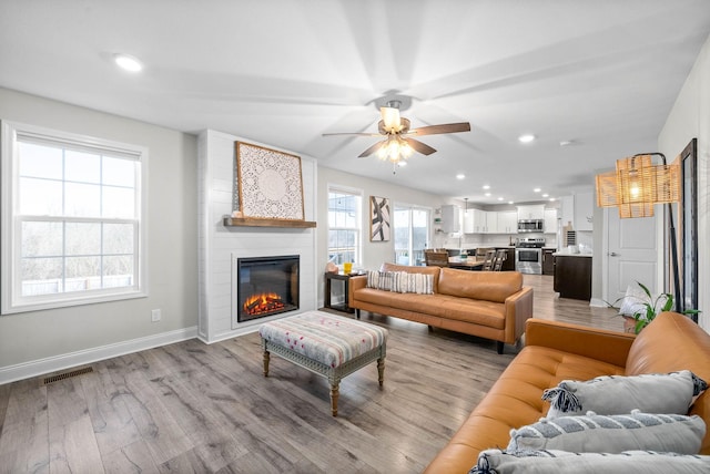 living room with a fireplace, light wood-type flooring, and ceiling fan