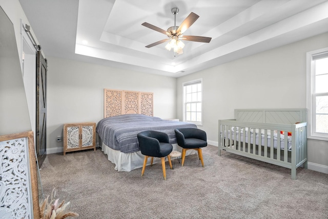 bedroom featuring ceiling fan, a tray ceiling, carpet floors, and a barn door