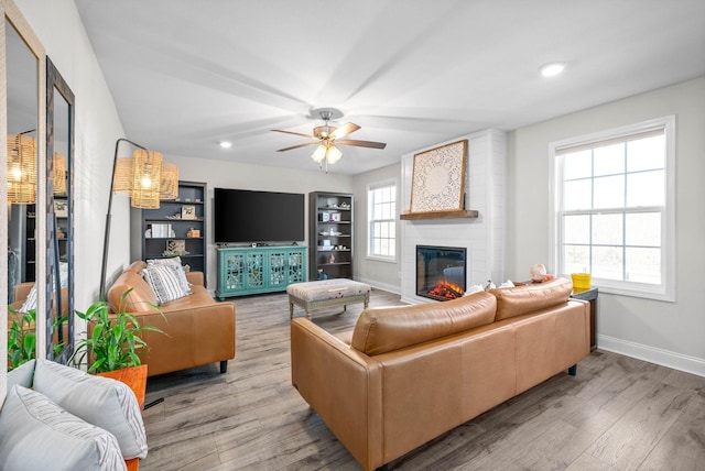 living room with ceiling fan, a large fireplace, and light hardwood / wood-style flooring