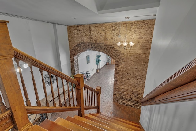 stairway featuring brick wall and an inviting chandelier