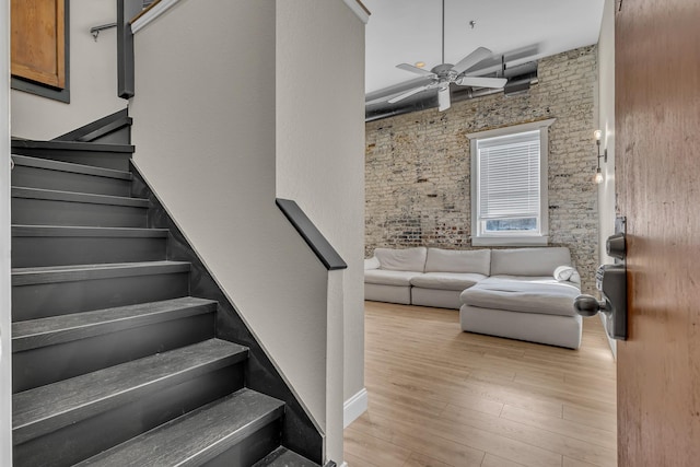 stairs with ceiling fan, brick wall, and hardwood / wood-style flooring