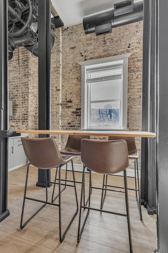 dining area featuring brick wall and light hardwood / wood-style flooring