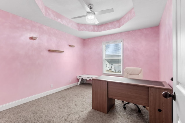 office area with light carpet, a tray ceiling, and ceiling fan