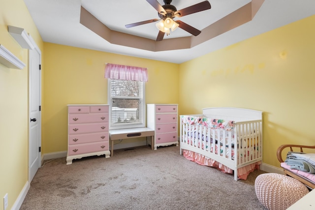 carpeted bedroom with a crib, a raised ceiling, and ceiling fan