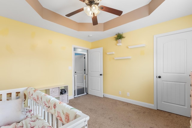 bedroom featuring light carpet, a tray ceiling, and ceiling fan