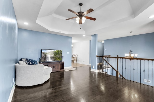 living area featuring dark wood-type flooring, a tray ceiling, and ceiling fan with notable chandelier