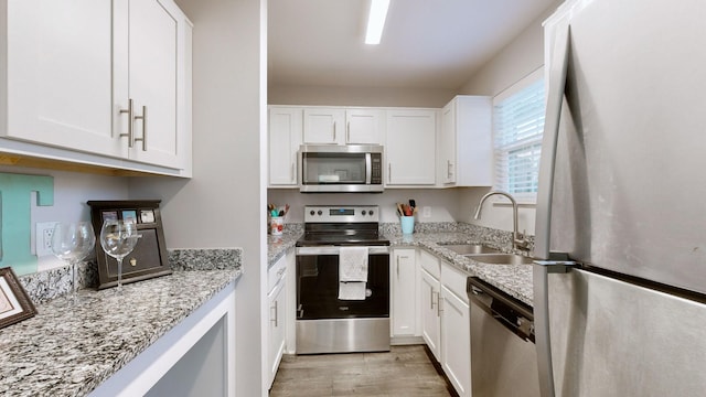 kitchen with light stone countertops, sink, stainless steel appliances, and white cabinetry