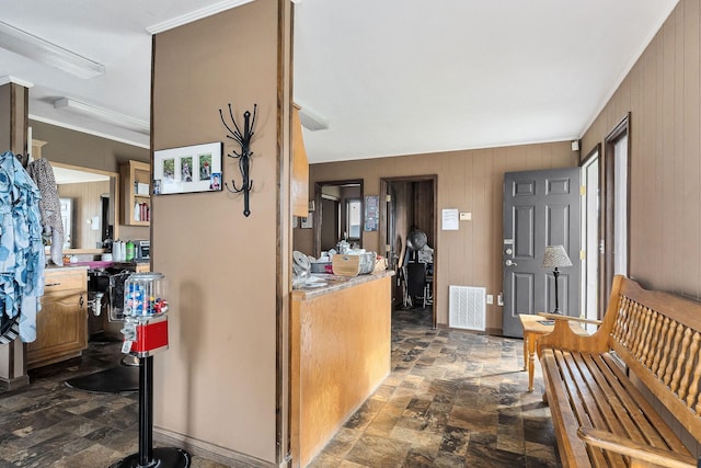 entryway with ornamental molding and wood walls