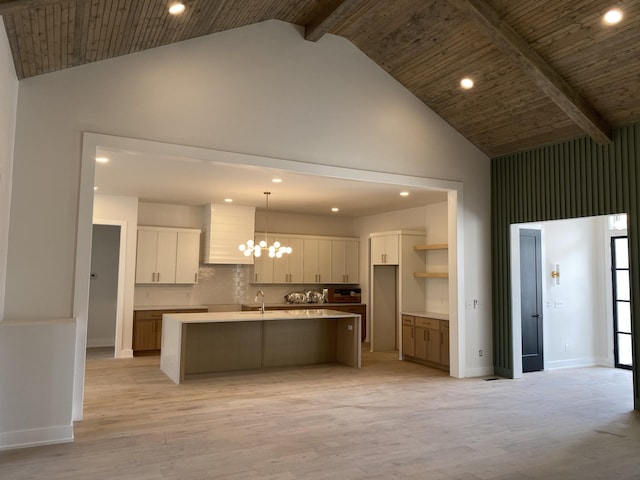 kitchen featuring a kitchen island with sink, white cabinets, hanging light fixtures, high vaulted ceiling, and light hardwood / wood-style flooring