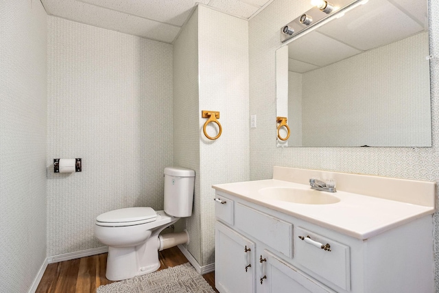 bathroom with hardwood / wood-style flooring, toilet, vanity, and a paneled ceiling