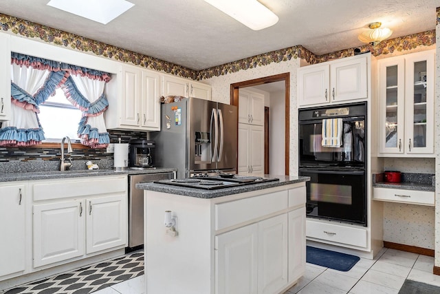 kitchen featuring a center island, black appliances, sink, white cabinetry, and a skylight