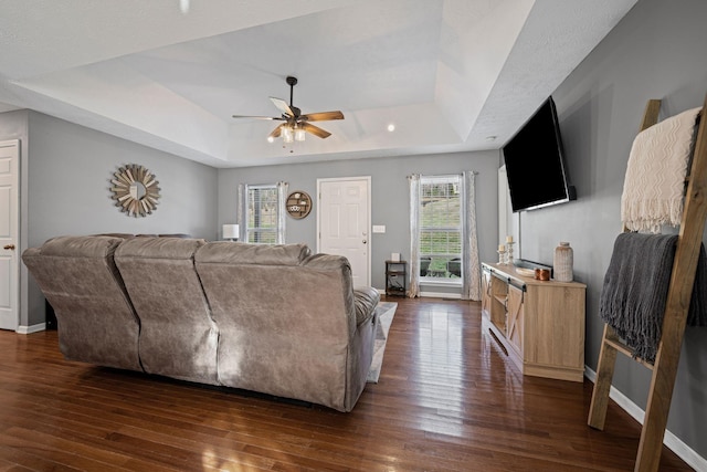 living room with ceiling fan, dark hardwood / wood-style floors, and a tray ceiling