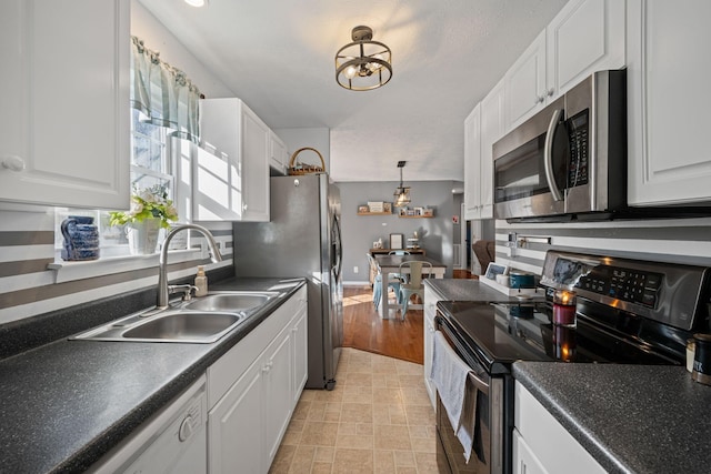 kitchen with sink, stainless steel appliances, white cabinets, and decorative light fixtures