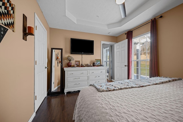 bedroom with ceiling fan, a raised ceiling, dark hardwood / wood-style floors, and a textured ceiling