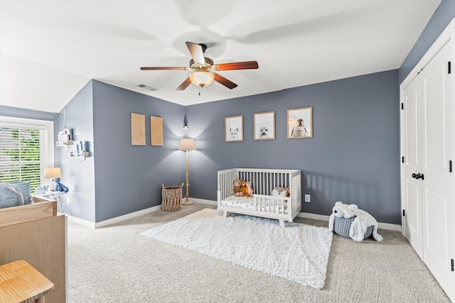 carpeted bedroom with ceiling fan, a nursery area, and lofted ceiling