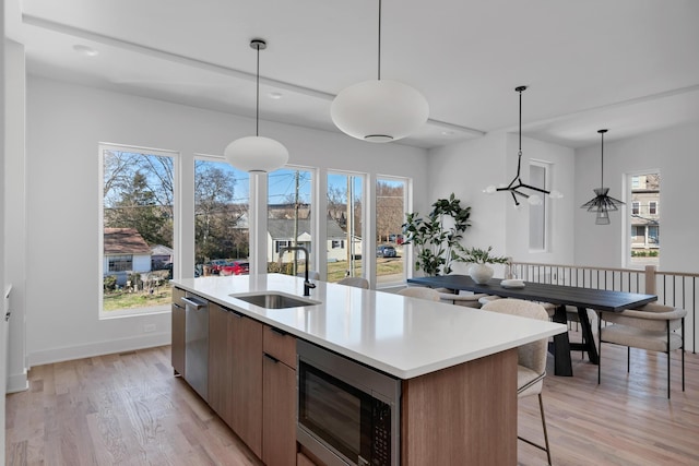 kitchen with sink, a center island with sink, hanging light fixtures, and appliances with stainless steel finishes