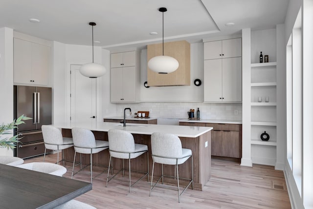 kitchen featuring high end fridge, decorative light fixtures, light hardwood / wood-style flooring, and an island with sink