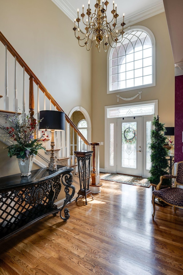 foyer with hardwood / wood-style flooring, ornamental molding, a chandelier, and a high ceiling