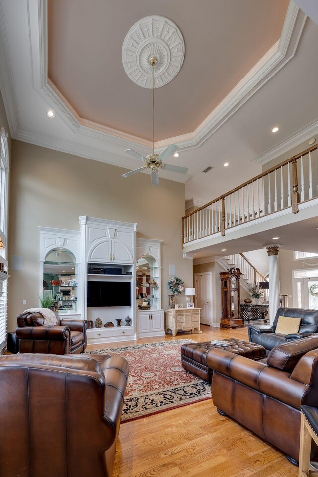 living room with a raised ceiling, crown molding, a high ceiling, and light hardwood / wood-style floors