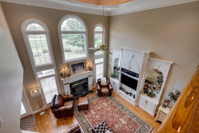 living room with light hardwood / wood-style flooring, ceiling fan, a towering ceiling, a fireplace, and ornamental molding