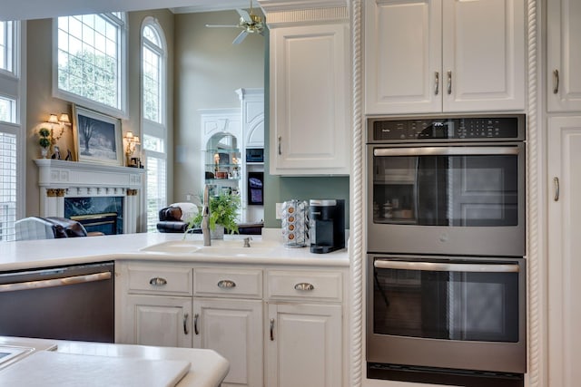 kitchen featuring sink, a premium fireplace, appliances with stainless steel finishes, white cabinetry, and a high ceiling