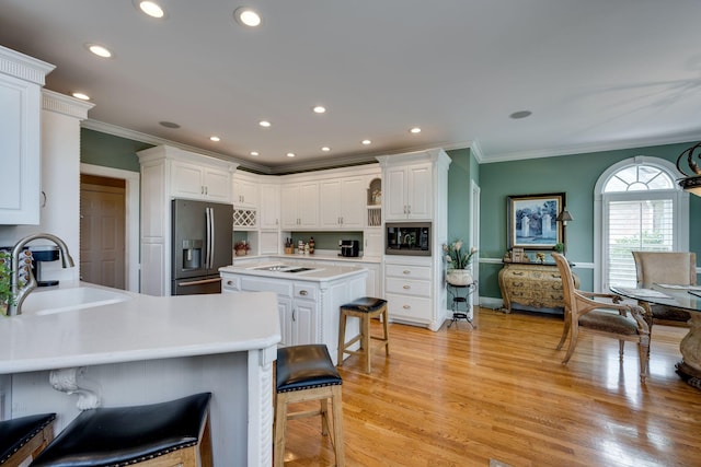 kitchen with a kitchen island, a breakfast bar, white cabinetry, sink, and black appliances