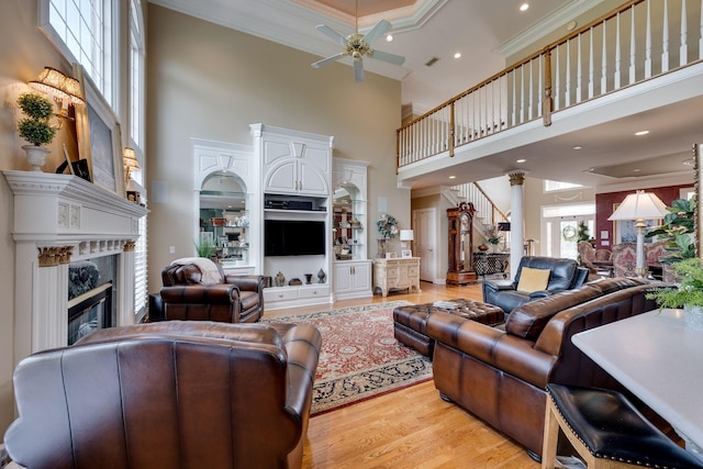 living room with crown molding, light wood-type flooring, ceiling fan, a fireplace, and a high ceiling