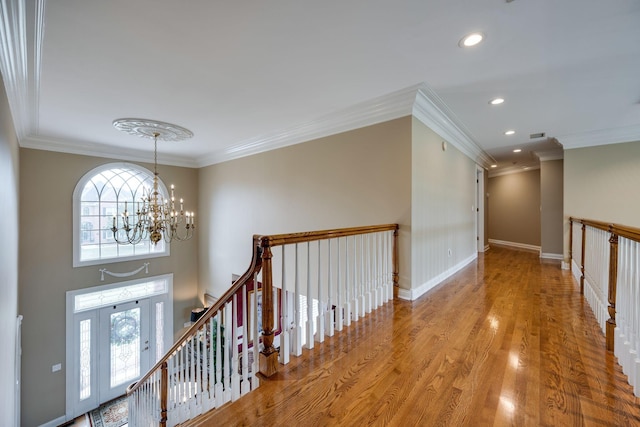 corridor with ornamental molding, plenty of natural light, light hardwood / wood-style floors, and a notable chandelier