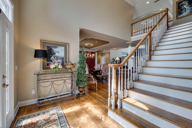 foyer entrance with an inviting chandelier, ornamental molding, a high ceiling, and light wood-type flooring