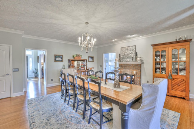 dining room featuring a textured ceiling, light hardwood / wood-style flooring, ornamental molding, and a fireplace