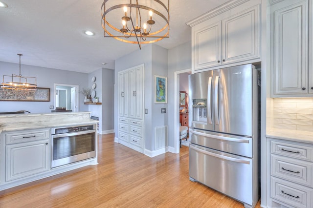 kitchen with tasteful backsplash, decorative light fixtures, light stone countertops, stainless steel appliances, and a chandelier