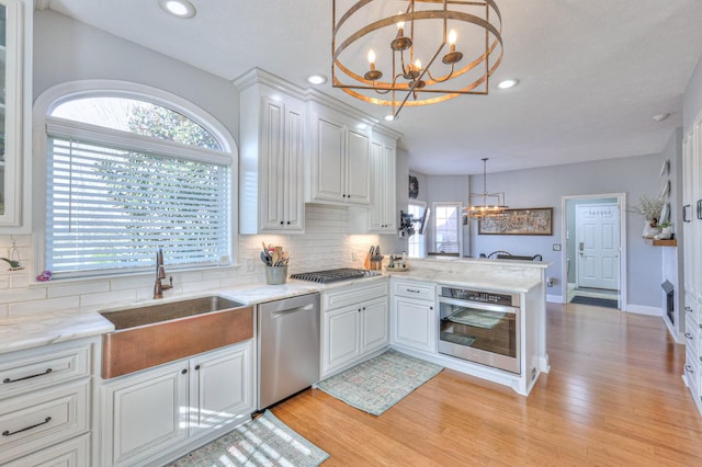 kitchen featuring decorative light fixtures, white cabinetry, stainless steel appliances, sink, and kitchen peninsula