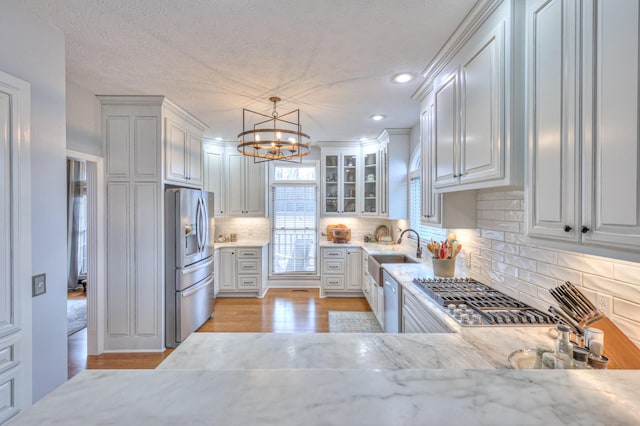 kitchen featuring light stone countertops, appliances with stainless steel finishes, decorative light fixtures, white cabinetry, and sink