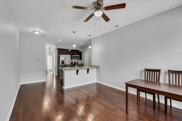 kitchen featuring ceiling fan, kitchen peninsula, a kitchen breakfast bar, stainless steel appliances, and light stone counters