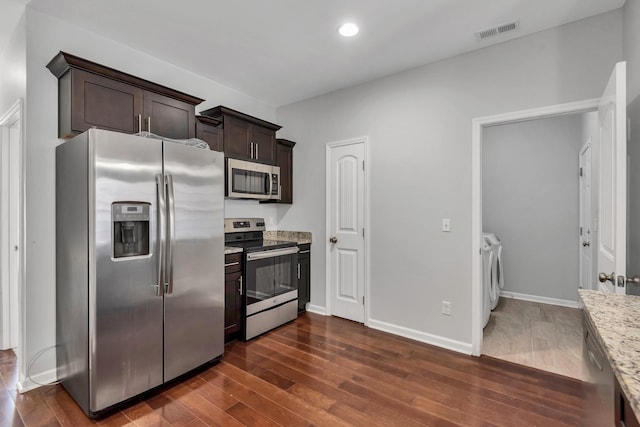 kitchen with light stone countertops, appliances with stainless steel finishes, washing machine and dryer, dark wood-type flooring, and dark brown cabinets