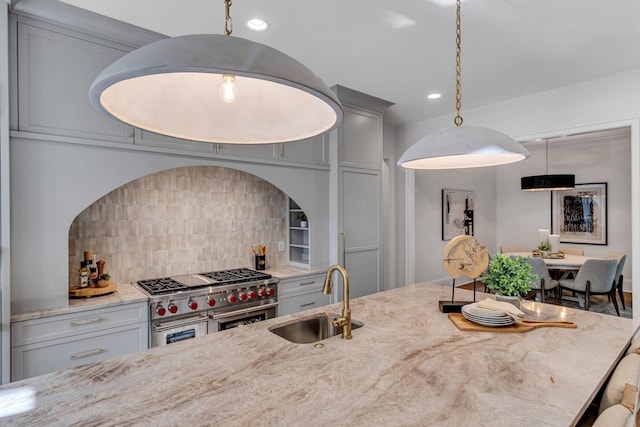 kitchen with backsplash, decorative light fixtures, range with two ovens, light stone countertops, and sink